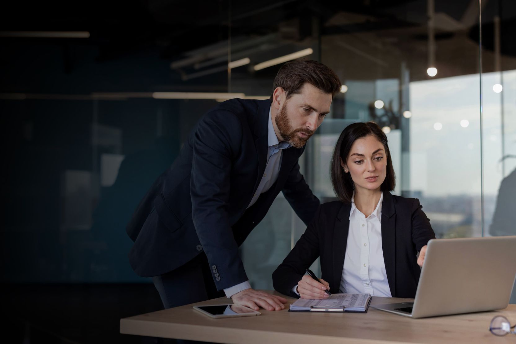 Business professionals discussing strategy while working on a laptop in a corporate office.