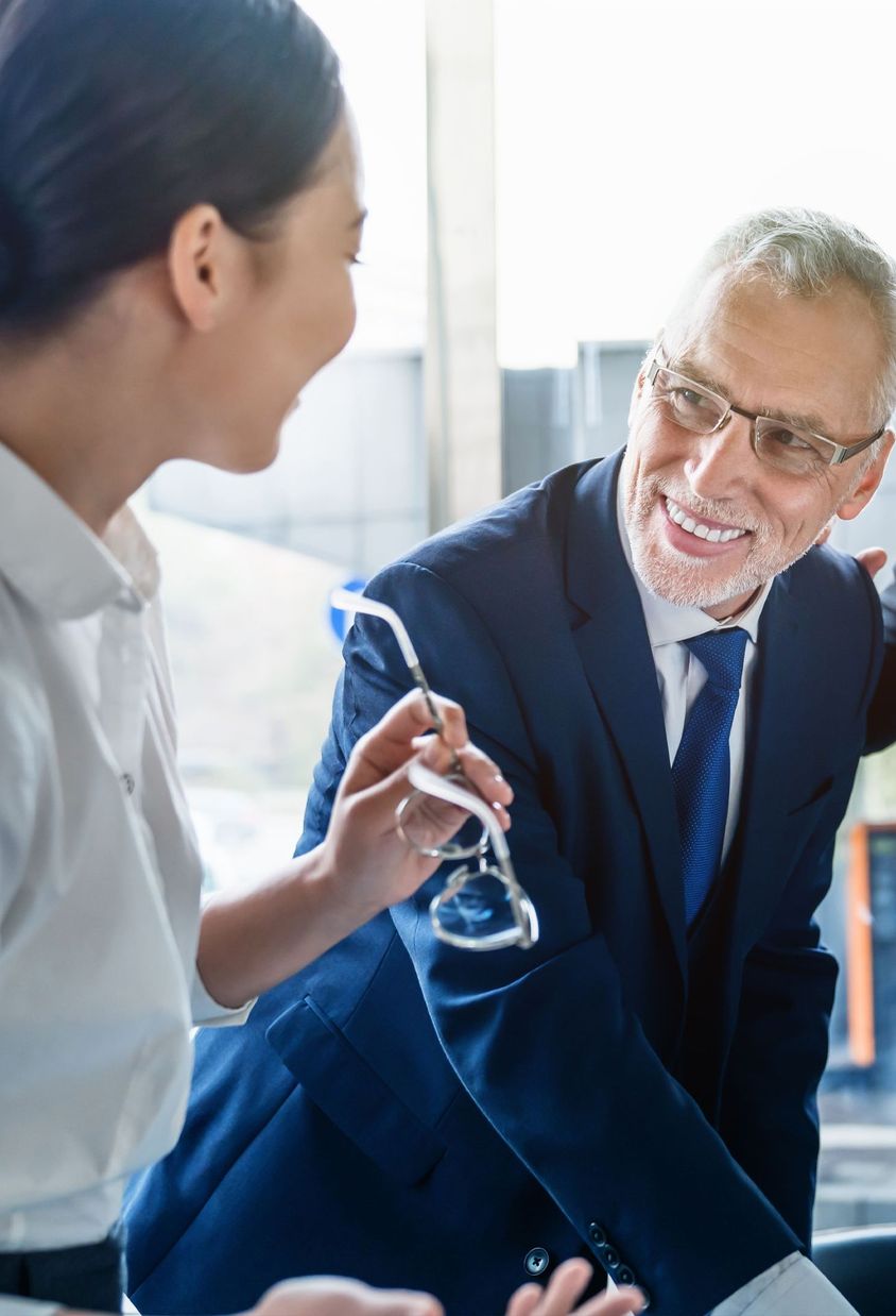 A group of diverse professionals in formal attire smiling and interacting in a modern office.